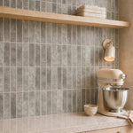 MORCART MT2209-XPE warm taupe grey vertical linear wall tiles, oblique kitchen detail with an oak shelf and cream mixer, fine mottled print and a shallow glossy finish.
