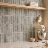 MORCART MT2209-XPE warm taupe grey vertical linear wall tiles, oblique kitchen detail with an oak shelf and cream mixer, fine mottled print and a shallow glossy finish.