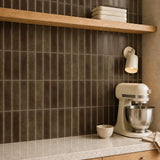 MORCART MT2415-XPE deep cocoa brown vertical linear wall tiles, oblique kitchen detail with an oak shelf and cream mixer, fine mottled print and a shallow glossy finish.